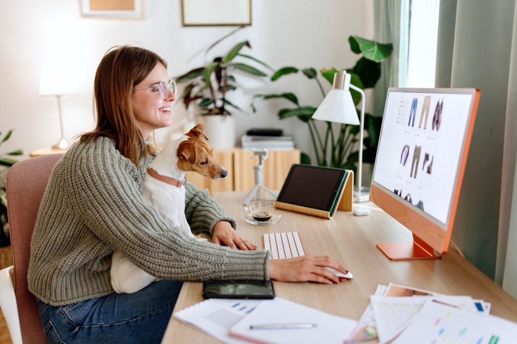 Woman sitting with her dog at table using desktop computer for online shopping